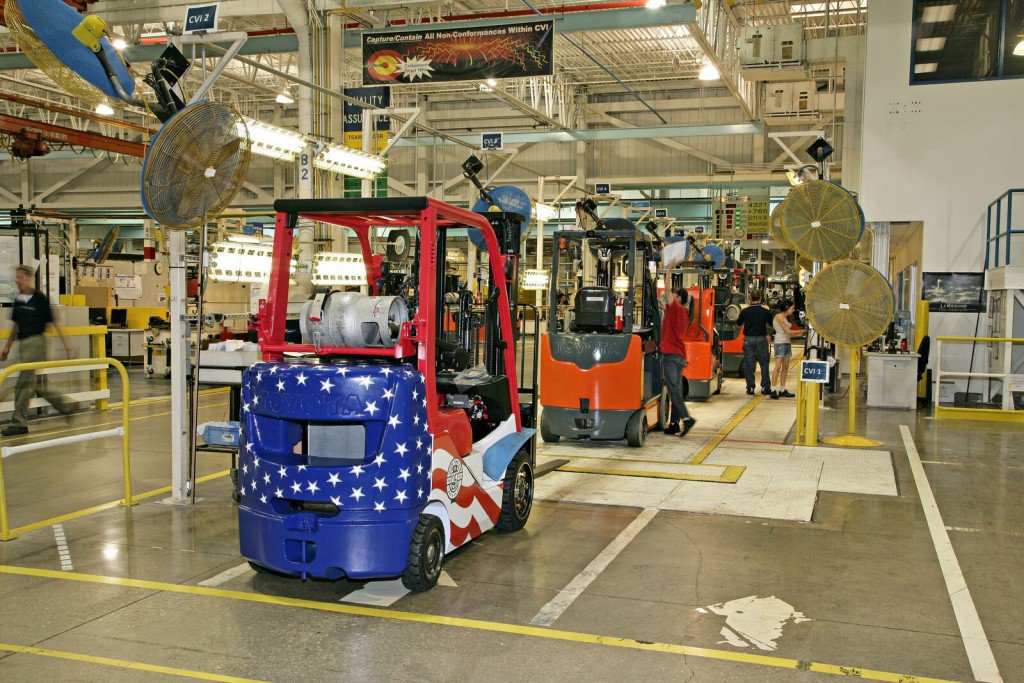 Many forklifts lined up in warehouse, with the forklift in the front being painted to look like the USA flag 