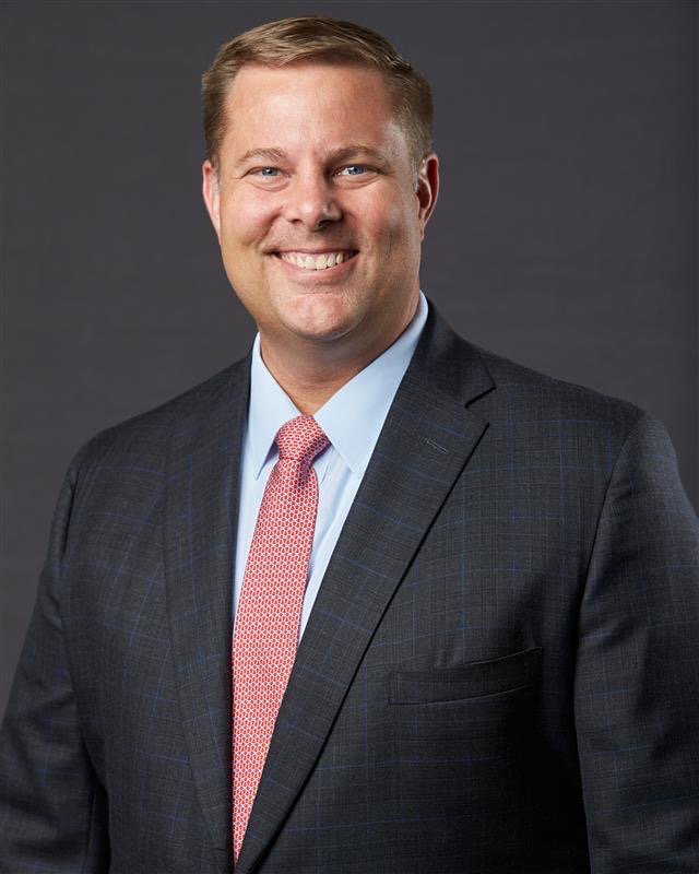 Mark Taggart headshot. Wearing grey suit and red tie