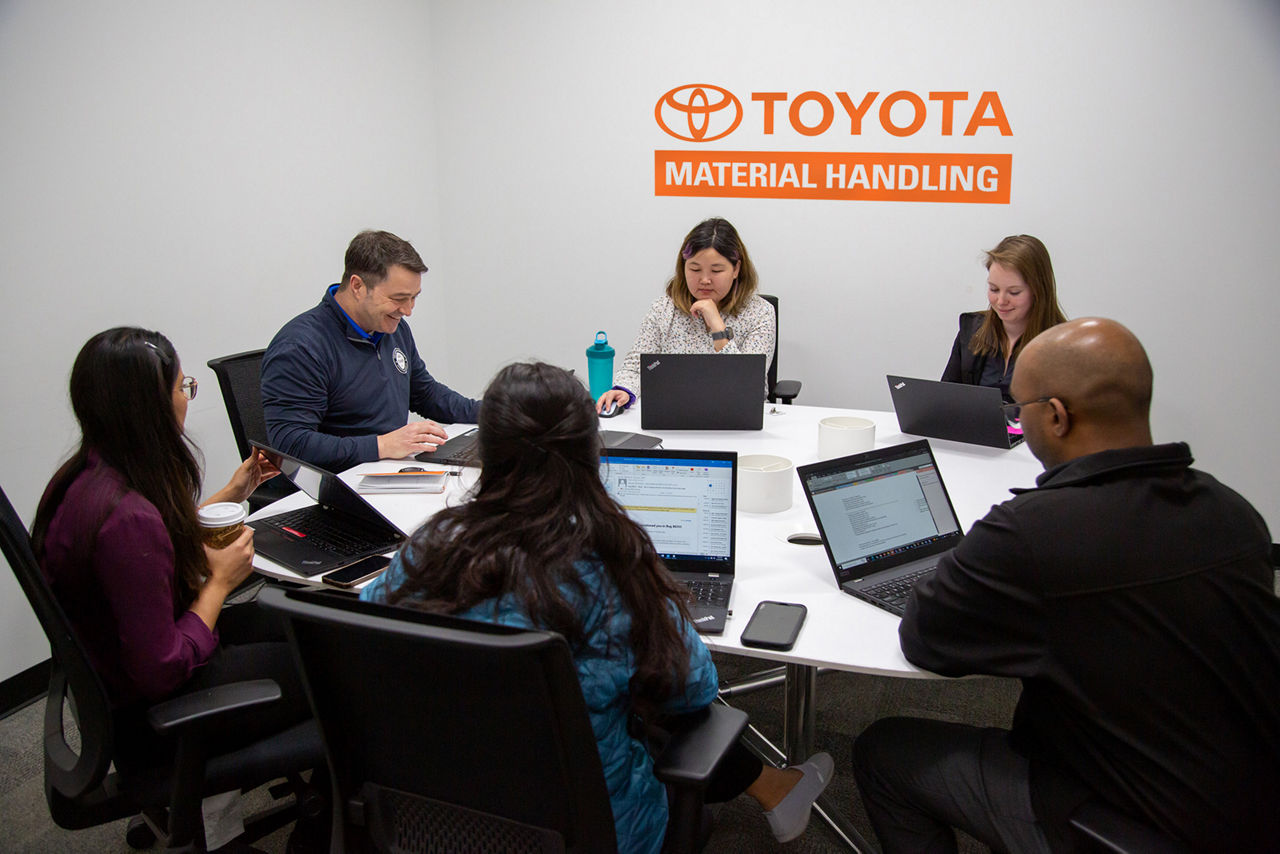 two men and four women sitting at a conference room table having a meeting